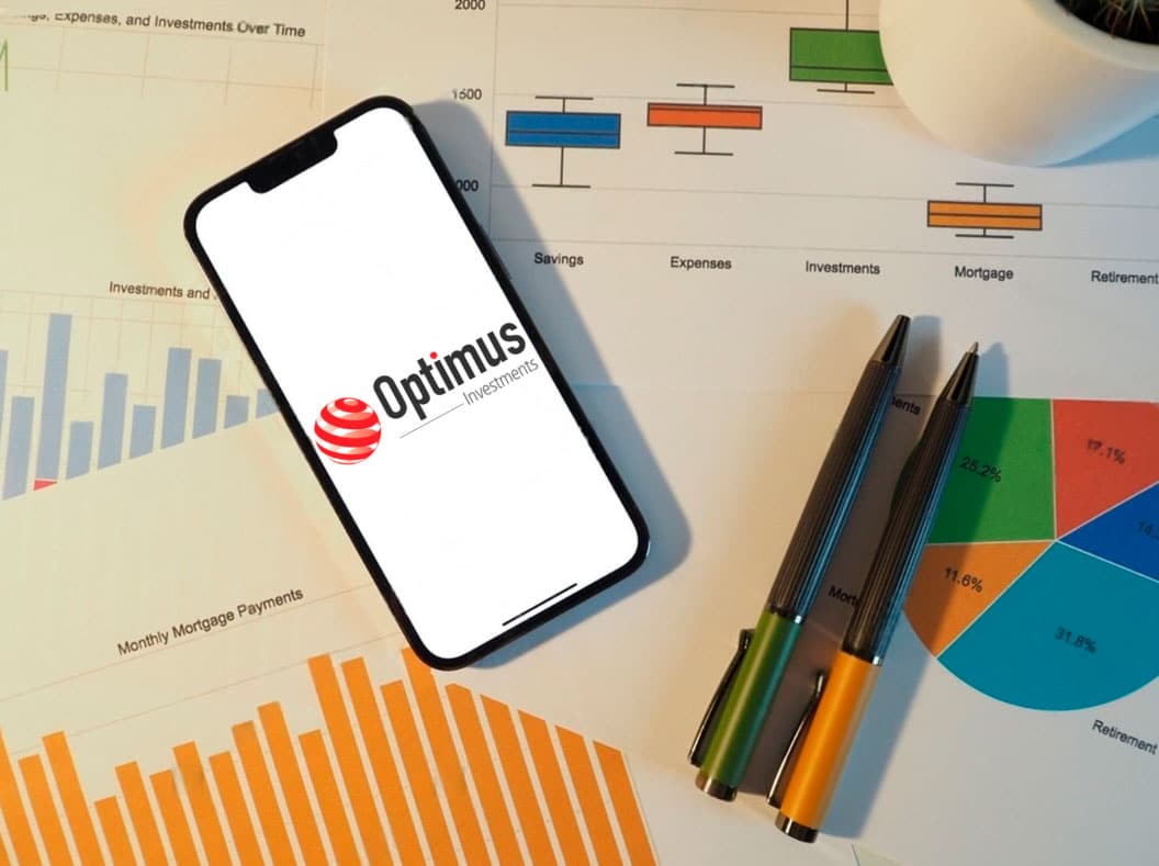 Teléfono mobil con logo de Optimus Investments encima de unas hojas con estadisticas y graficos