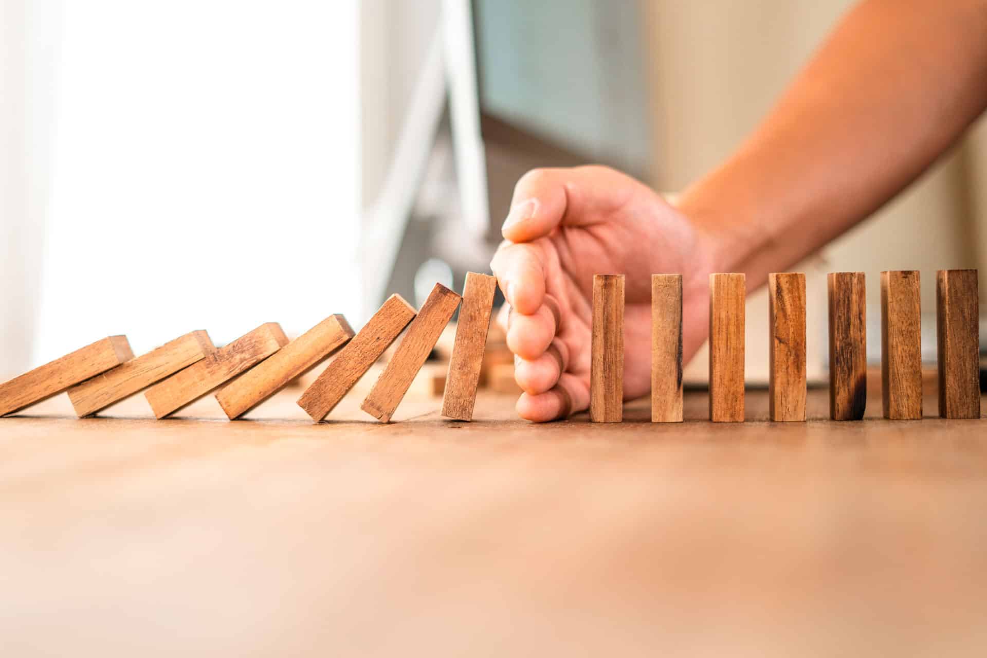 Fichas del domino en fila cayendo y una mano que lo bloquea por la mitad del recorrido